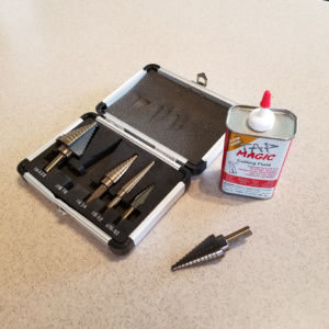 Step Drill Bits come in kits like this one, or you can buy them individually. They come in a variety of sizes and drill holes larger and larger in increments. Use cutting fluid while drilling to ease allow easier cutting.